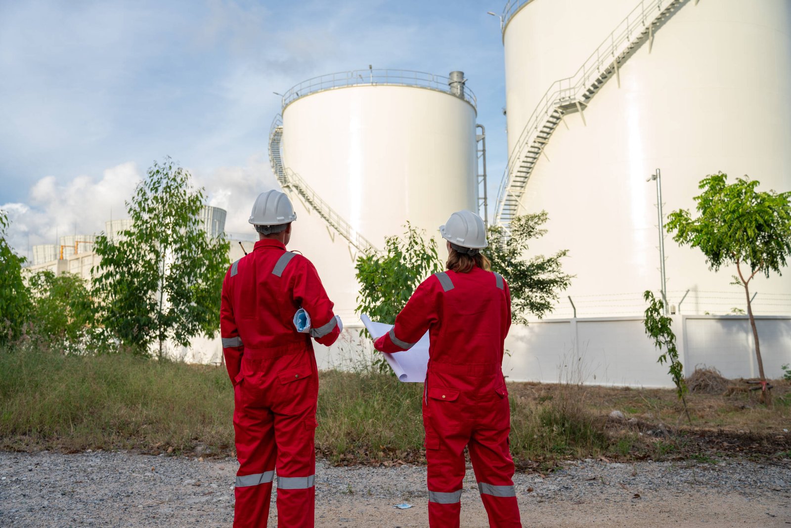 Team Electricity engineer discussion about blueprint drawings inside electricity power plant site. Senior Engineer wearing safety jacket and PPE working about Petro Chemical plant